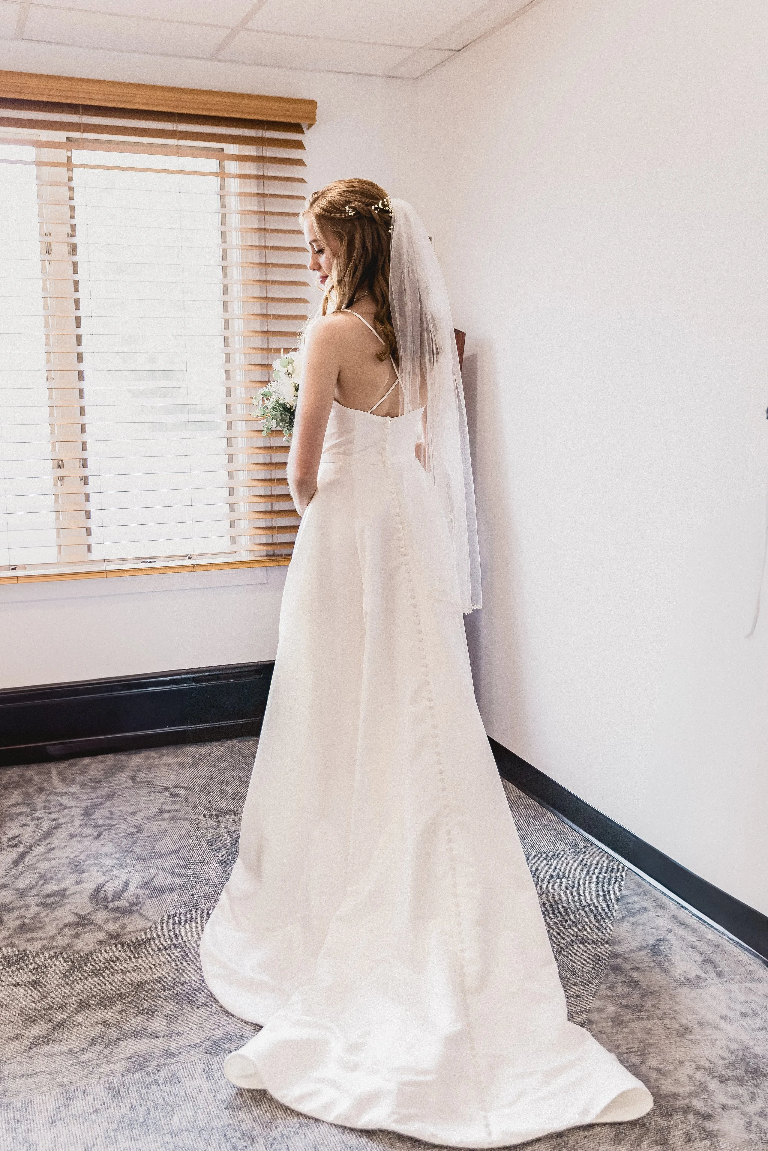 Bride seen from behind in window light, veil trailing