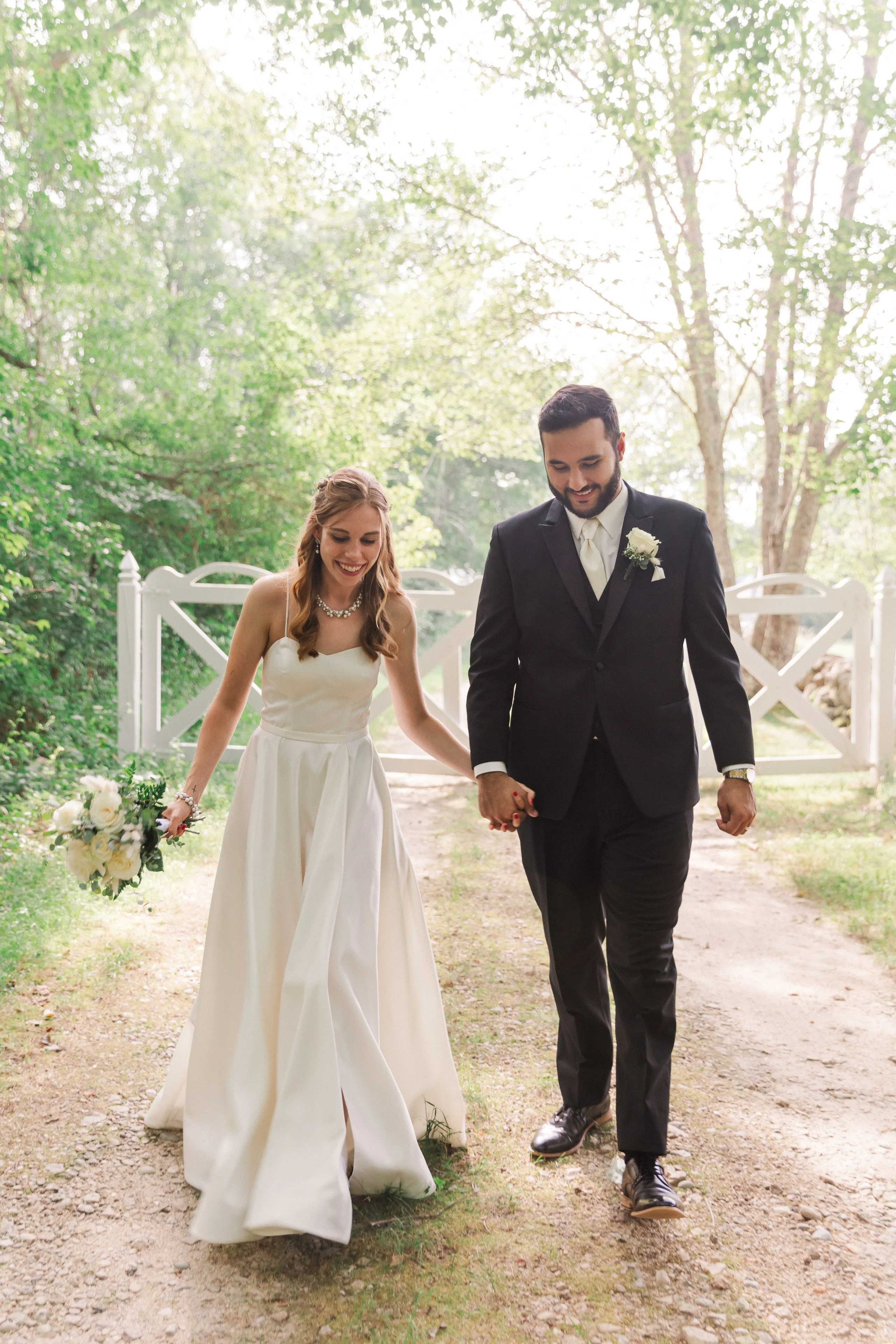 Couple walking hand in hand at a white gate at golden hour