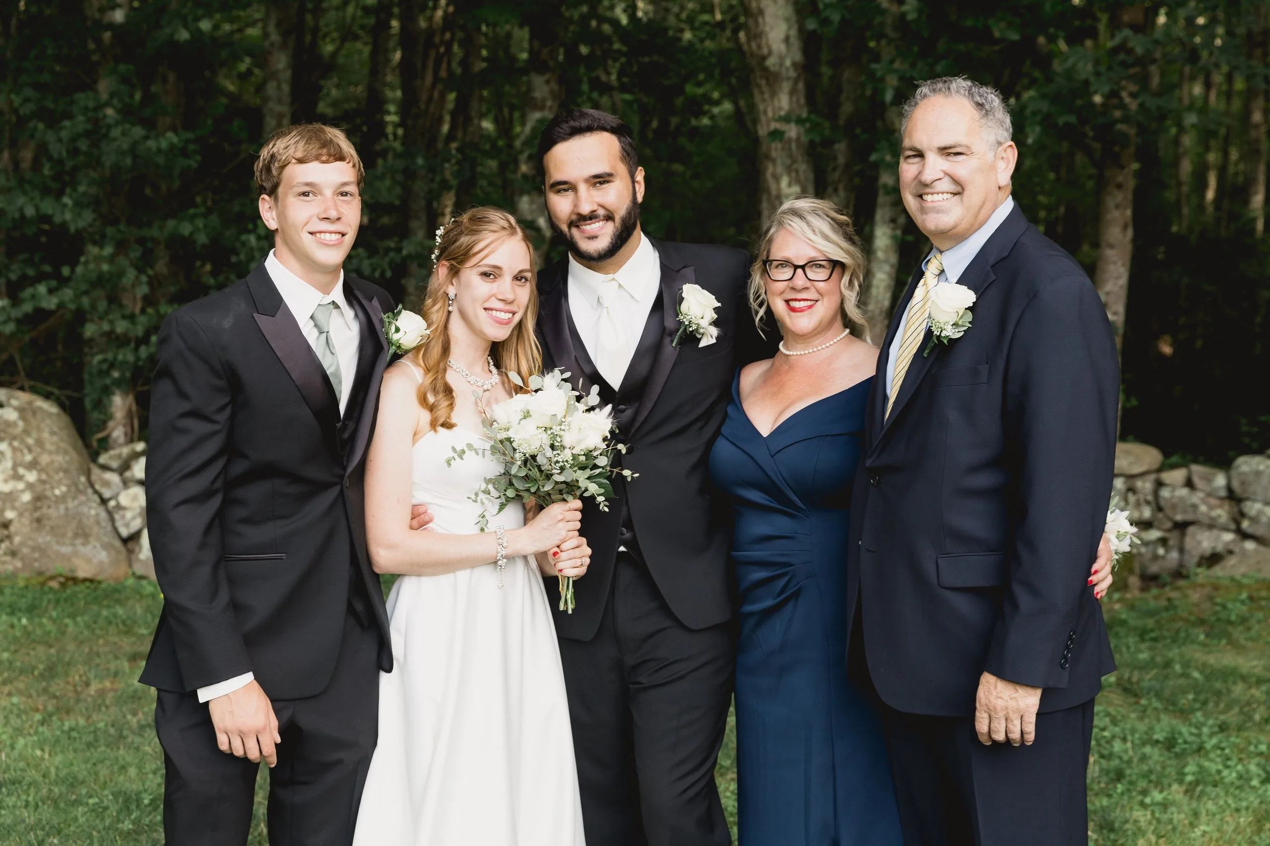 Bride and groom with family at a stone wall in the woods